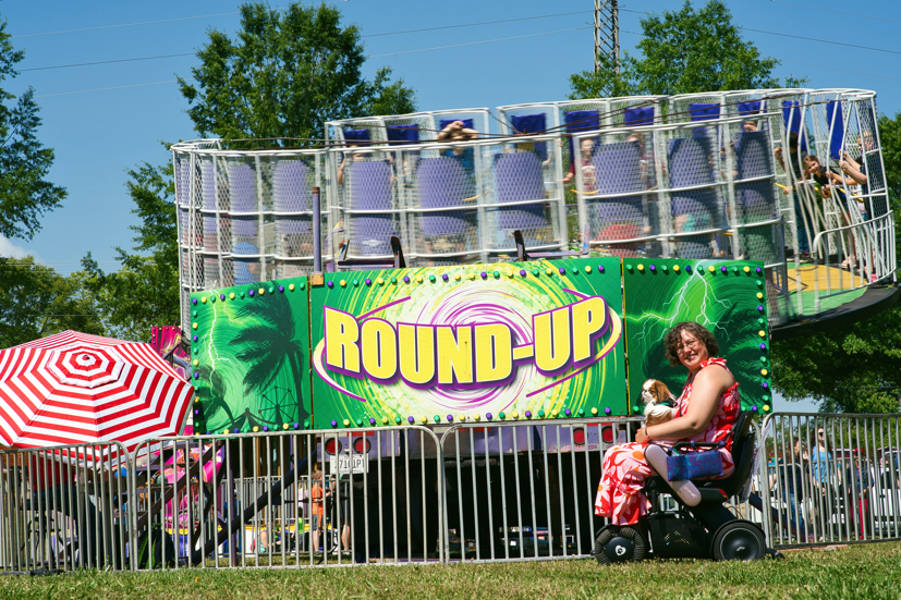 A Japanese Chin sits in the lap of a wheelchair user in front of an amusement park ride.